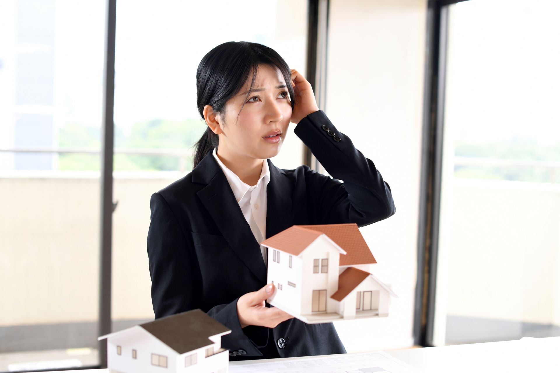 住宅模型を持ちながら悩むビジネスウーマン